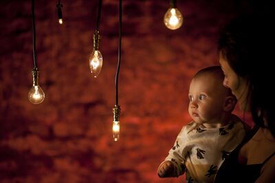 A woman holding her baby look on at 5 light bulbs that hang on black cables