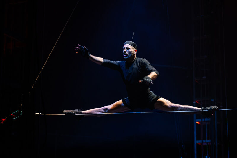 A man in a black outfit doing the splits on a tightrope
