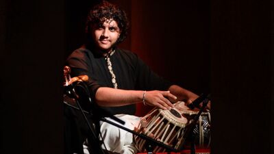 Man sits cross legged looking to the side and playing the tabla