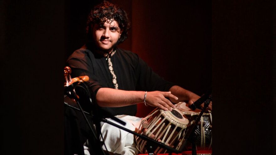 Man sits cross legged looking to the side and playing the tabla