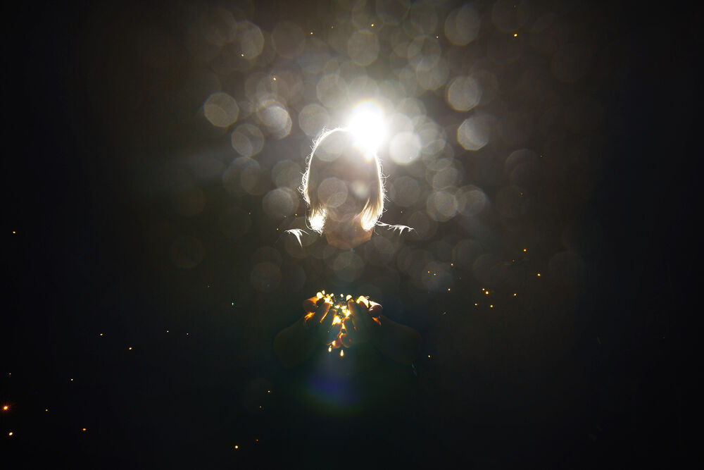 A person holds a bundle of fairylights in front of her, barely visible from a bright backlight and dust specks 