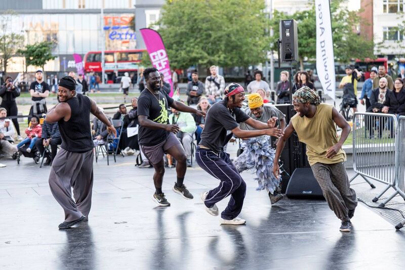 A group of five men joyfully run around an outdoor stage