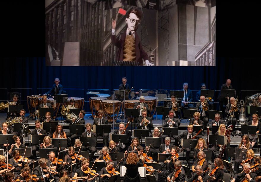 Brighton Philharmonic Orchestra playing on stage with a projection of William Kentridge's film 'Oh To Believe Another World'