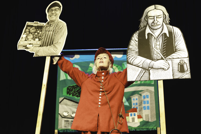 Victoria Melody stands with two cut-outs of historical figures raised about her head