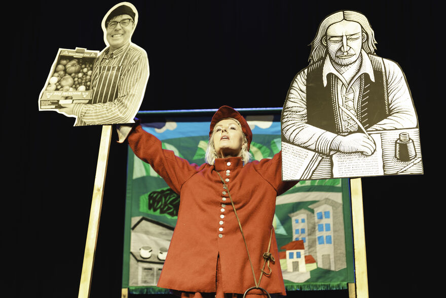 Victoria Melody stands with two cut-outs of historical figures raised about her head