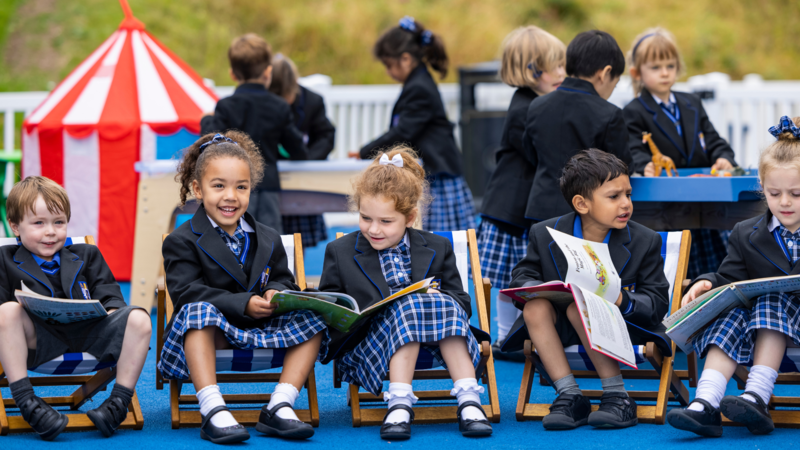 Young school kids sitting on small deckchairs, reading