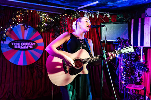 A woman in a black dress playing acoustic guitar and singing in to a microphone