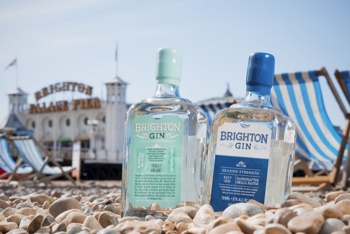 Two bottles of gin are nestled in pebbles, behind them are deckchairs and Brighton Palace Pier