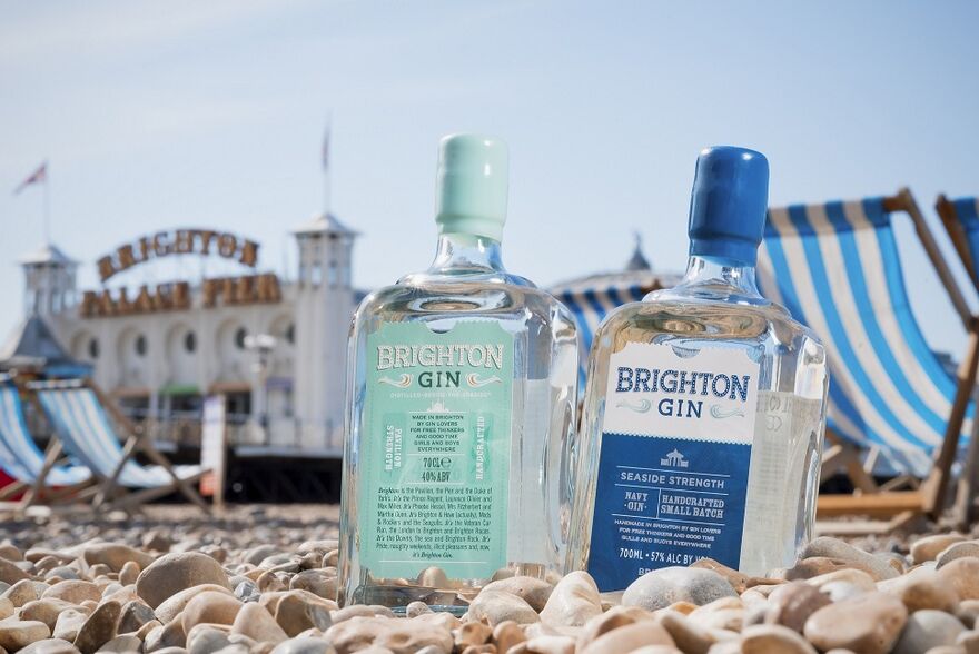 Two bottles of gin are nestled in pebbles, behind them are deckchairs and Brighton Palace Pier