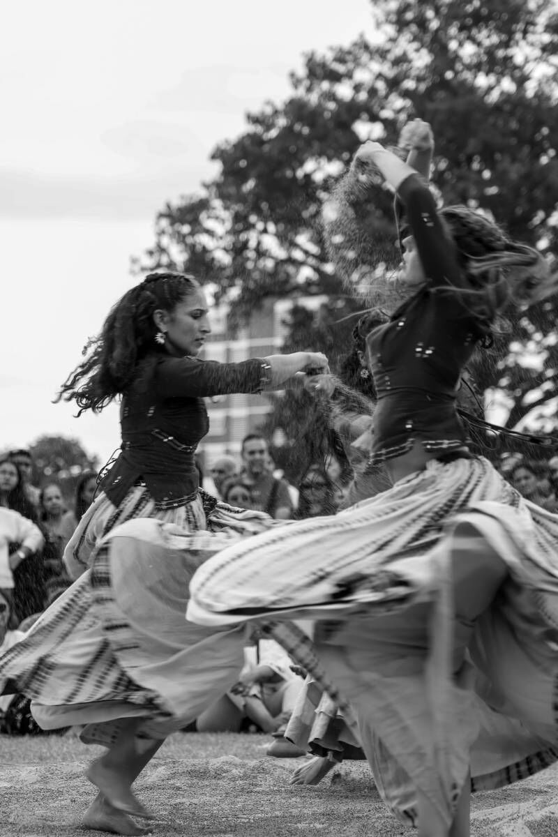 Two dancers spin with skirts twisting, sprinkling sand above their heads