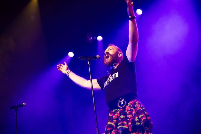 A performer stands with their arms raised singing into a mic