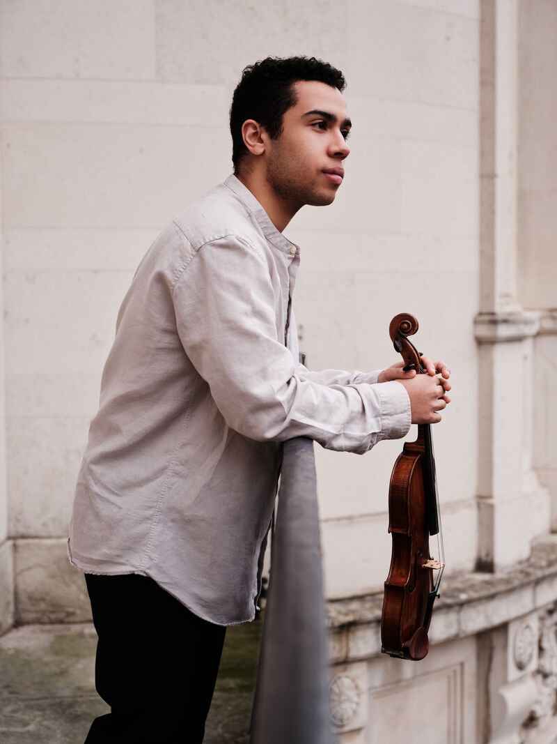 Jordan Brooks leaning over a railing holding his violin