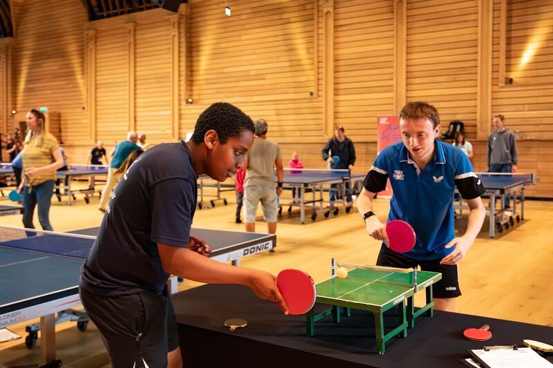 Two people play table tennis on a miniature sized table tennis table. They are both concentrating very hard