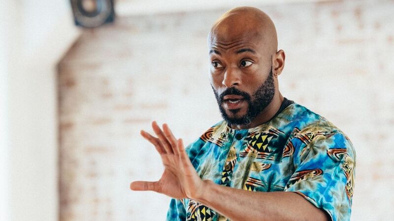 Arinze, a black man in a brightly patterned shirt, gestures with his left hand