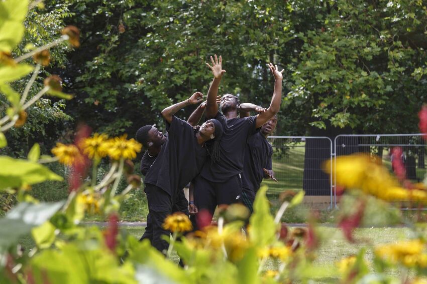 A group of men are dancing outside. They are seen through flowers