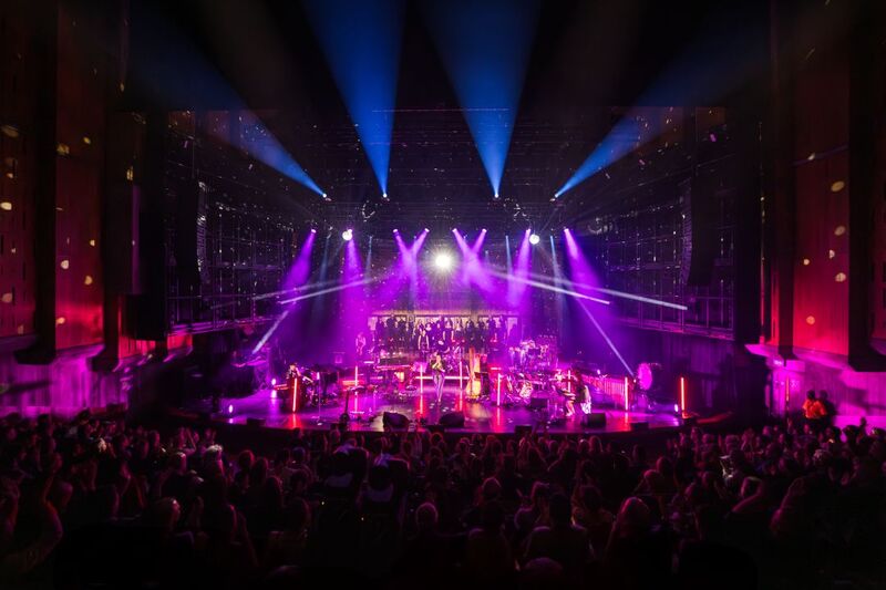 Picture from the back of the audience looking onto a colourful and brightly lit stage