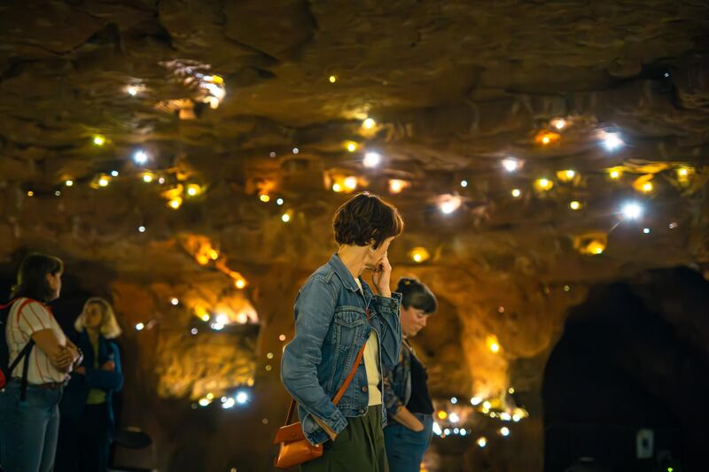 People stand around a cave with small lights scattered around the walls, floor and ceiling