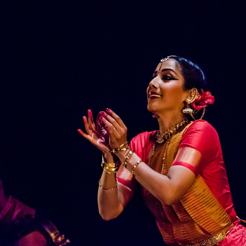 A dancer wearing gold bangles and a red dancer makes a flower shape with her hands