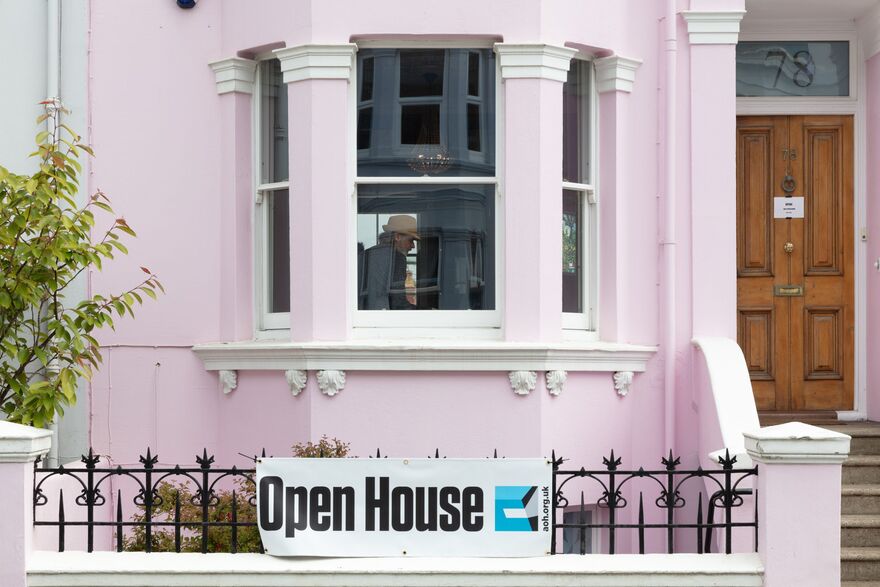 The front of a pink house with a bay window, on the black railings in front of the house is a sign that reads Open House
