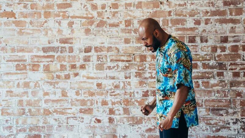 Arinze, a black man in a brightly patterned shirt, clenches his fists