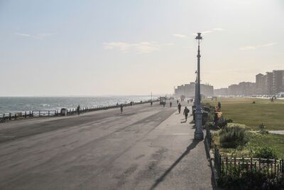 Hove Promenade with the sea on the left, a few silhouettes of people walking and a blue sunny sky