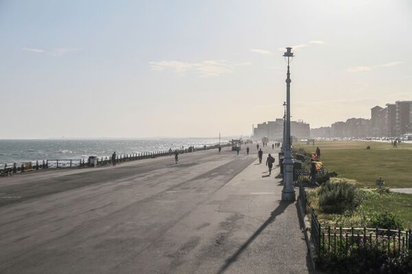 Hove Promenade with the sea on the left, a few silhouettes of people walking and a blue sunny sky