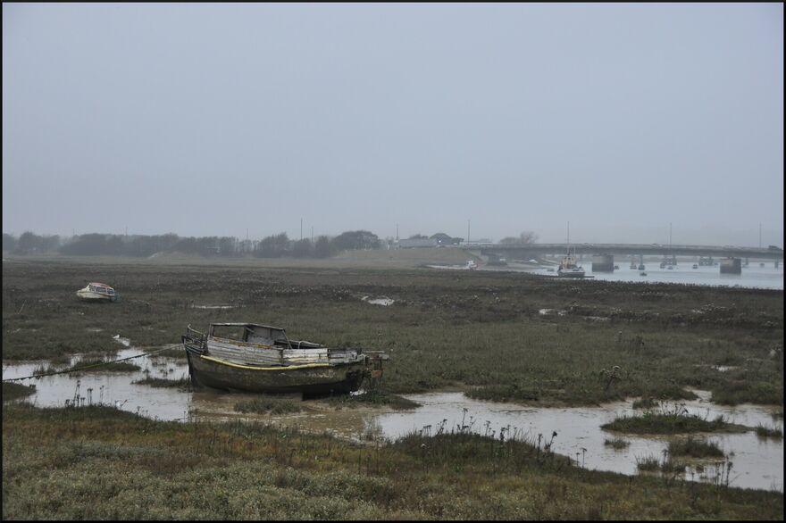 A small white boat sits on small stream of water, surrounded by marshland