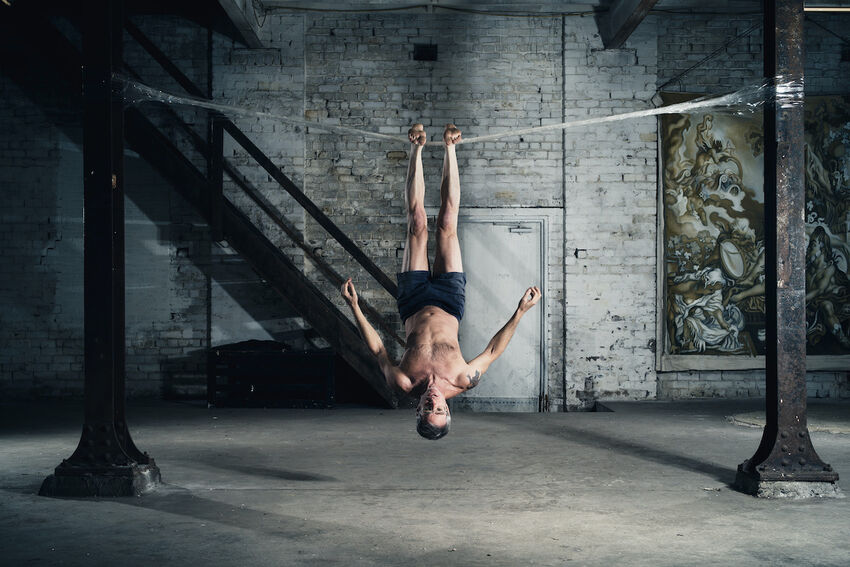 A person hangs upside-down by their feet from a line of packing tape