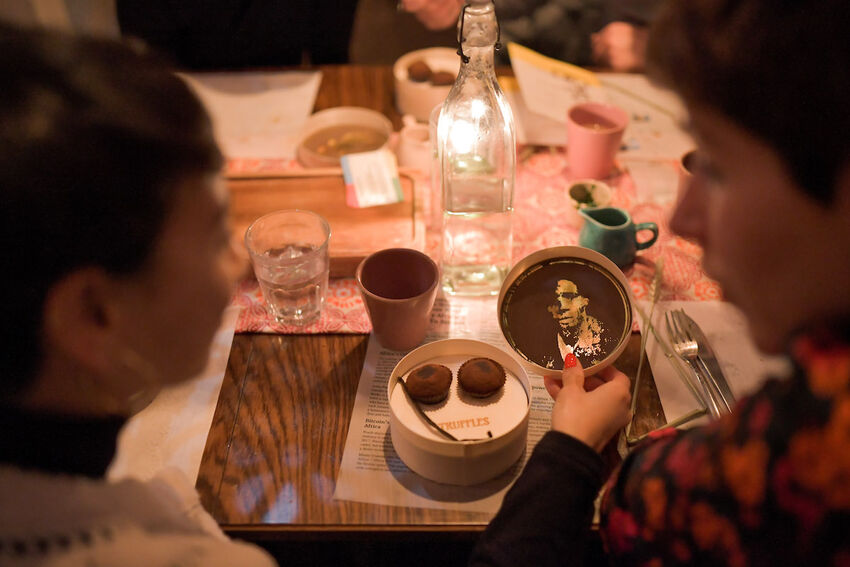 Looking over the shoulder of two people sat at a table with cups and food 