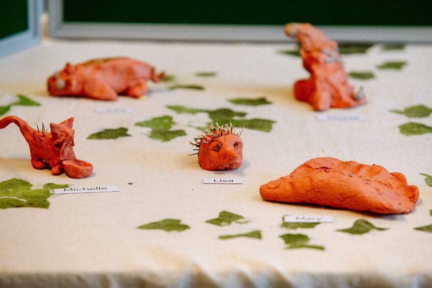 Some play-doh models of animals sit on a white table with bits of green leaves around them