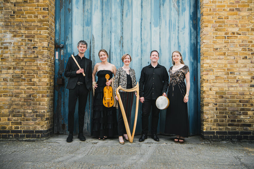 Five musicians stand in front of a blue doorway, holding a flue, harp, drum and violin