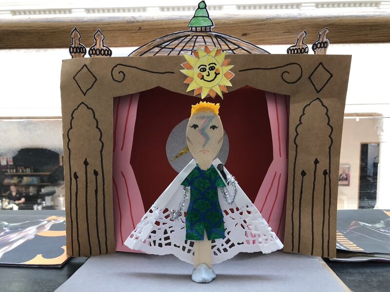 A papercraft Ziggy Stardust stands on a papercraft stage
