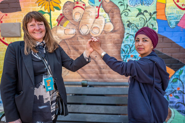 Two members of Brighton Festival staff shake hands, mimicking the mural wall behind them.