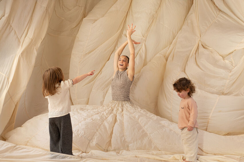 A dancer in an enormous skirt moves her arms as two young children delight in watching